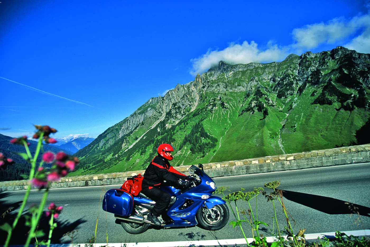 Motorrad auf der Arlbergstraße vor grün bewachsener Bergflanke